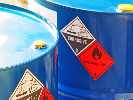 A closeup on two large, blue metal drums full of chemicals. There are warning stickers on the side of the drums.