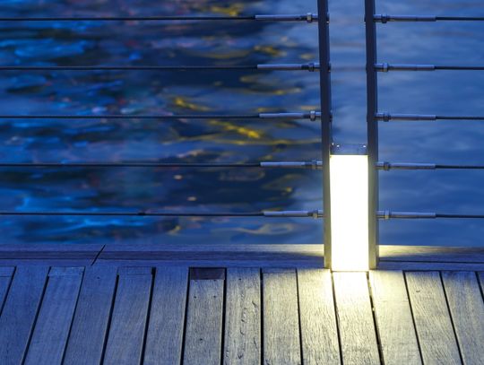 A wooden deck looks out over a body of water. Metal railing held together by cable runs along the deck.