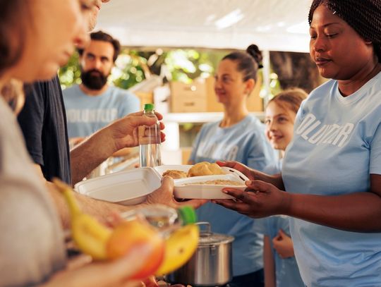 An outdoor food drive event where volunteers of diverse ethnicities serve individuals free food and water.