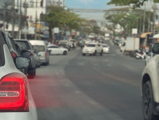 A close-up of the taillight of a white vehicle with its brakes on. A line of cars in a city is blurred ahead of the vehicle.