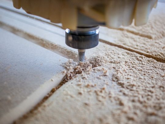 A CNC machine carves precise grooves into wood, scattering fine shavings during an active milling process.