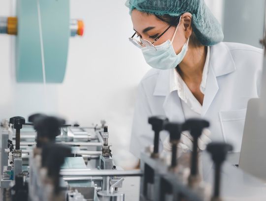 A professional woman doctor is wearing protective gear and glasses while working in a manufacturing setting.