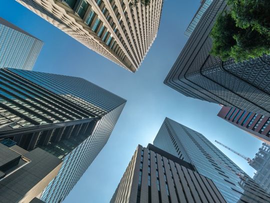 A ground-view looking up at several very tall buildings with multiple stories. The sky is clear and blue.