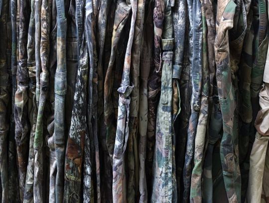 A rack full of camouflage pants in a store. All the pants have camo patterns, but some are lighter colors than others.