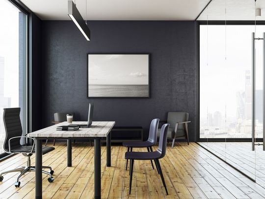An office with a piece of black-and-white art on the wall, and massive windows revealing a city skyline in the distance.