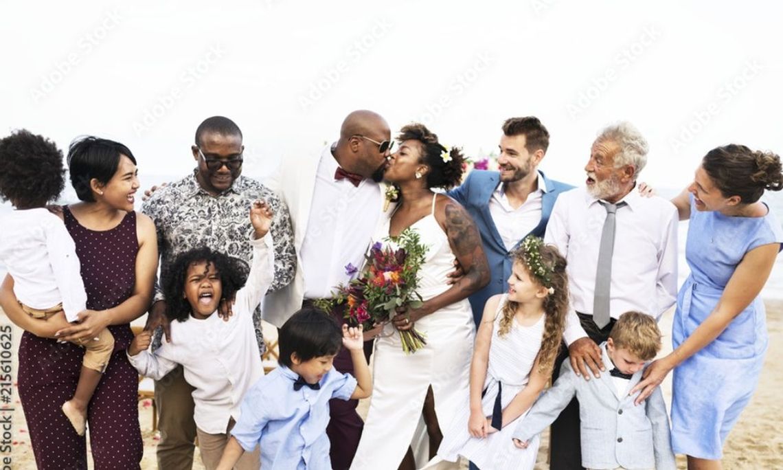 An African-American couple kiss on their wedding day. Their family surrounds them, smiling and cheering.