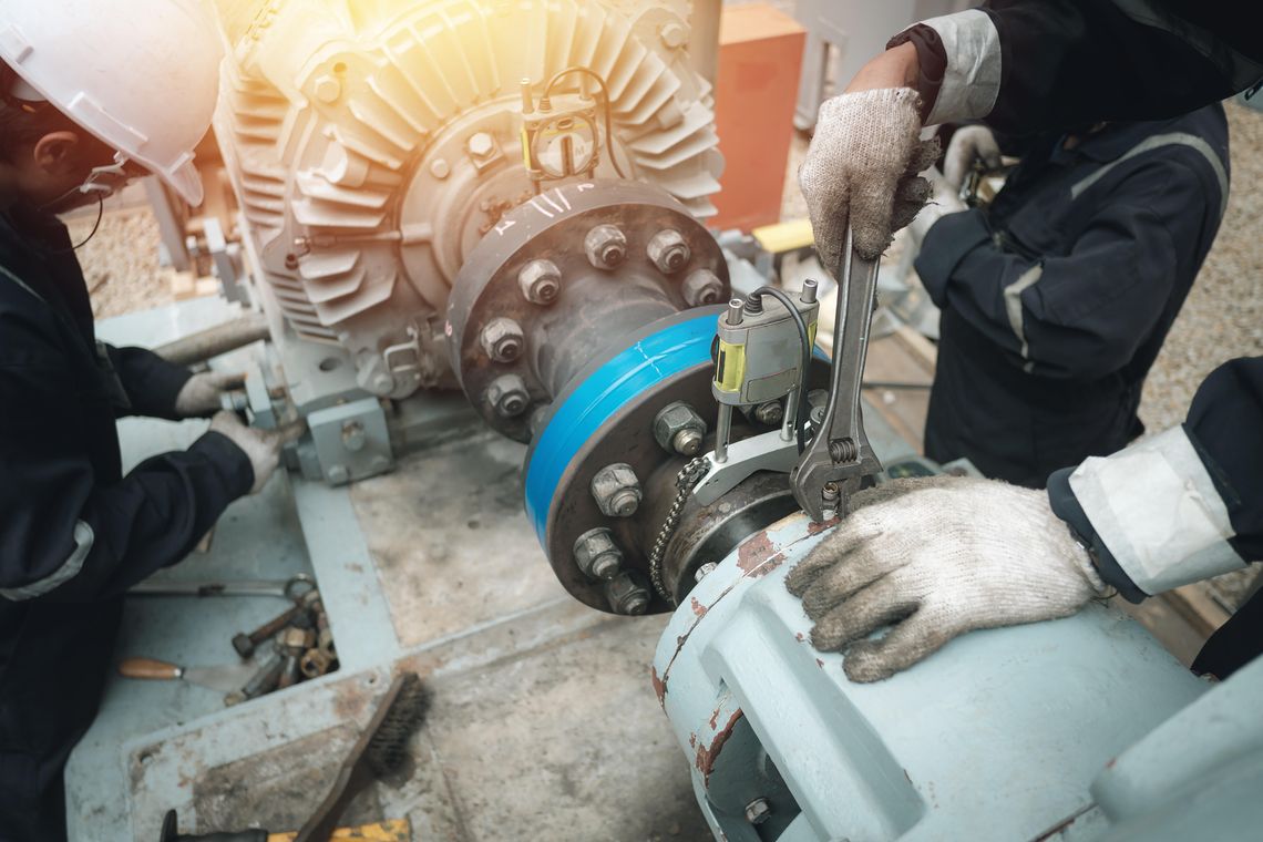 Two maintenance workers performing upkeep on the same piece of machinery while wearing white work gloves.