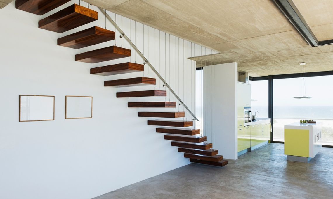 A floating staircase featuring dark red wood and a metal handrail in a modern, spacious, well-lit home