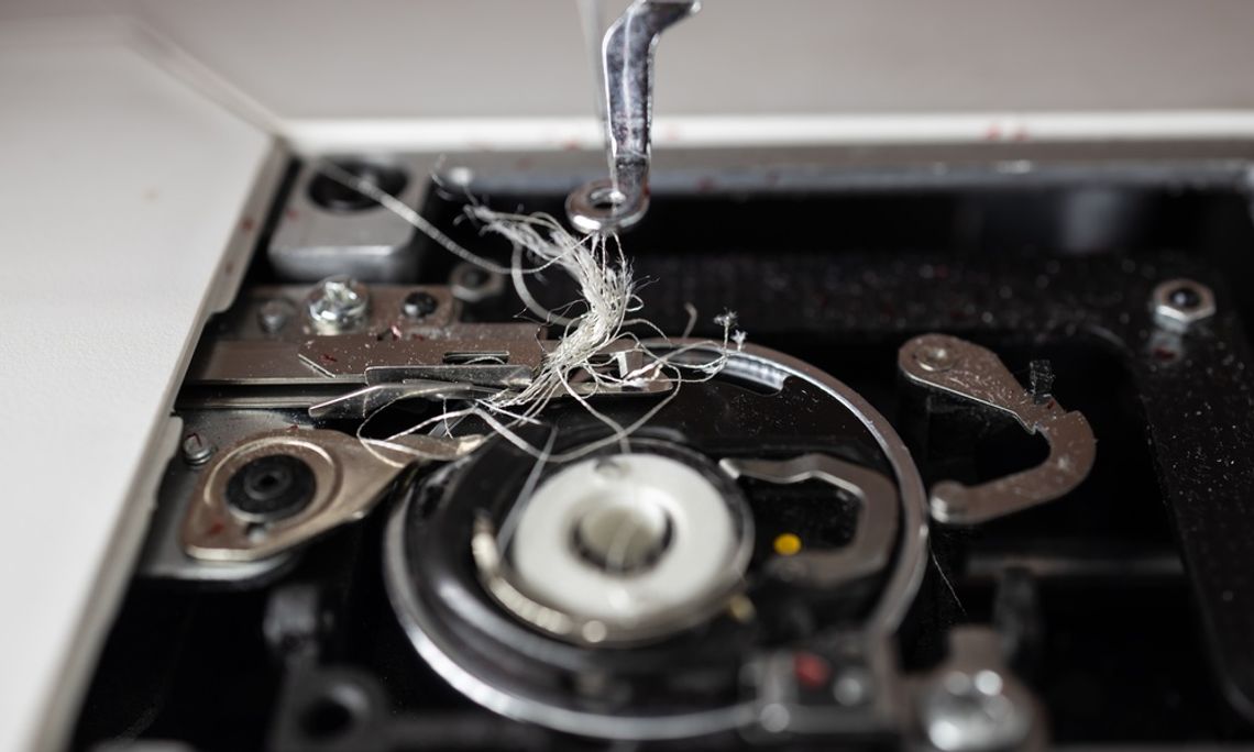 An extreme close-up shot of the interior of a sewing machine that holds the bobbin. It is tangled with white thread.