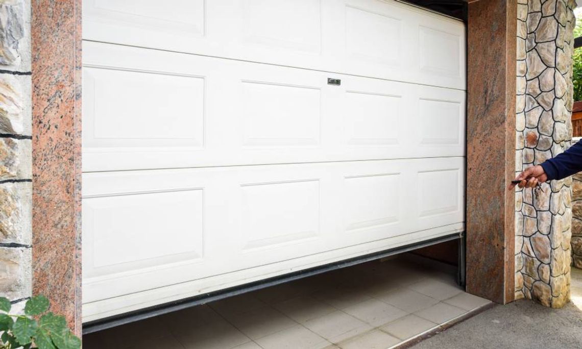 An individual is pointing a small garage door opener at a white garage door. The door is raised off the ground.