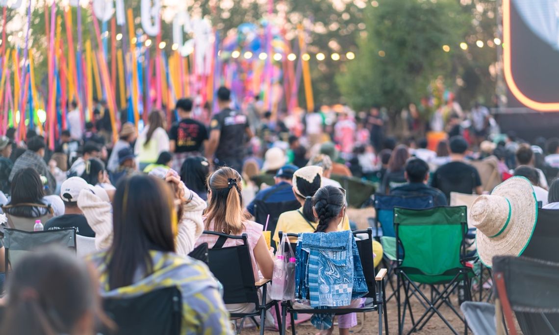 An overhead view of a crowd of people sitting on folding chairs in an outdoor area decorated with lights and streamers.