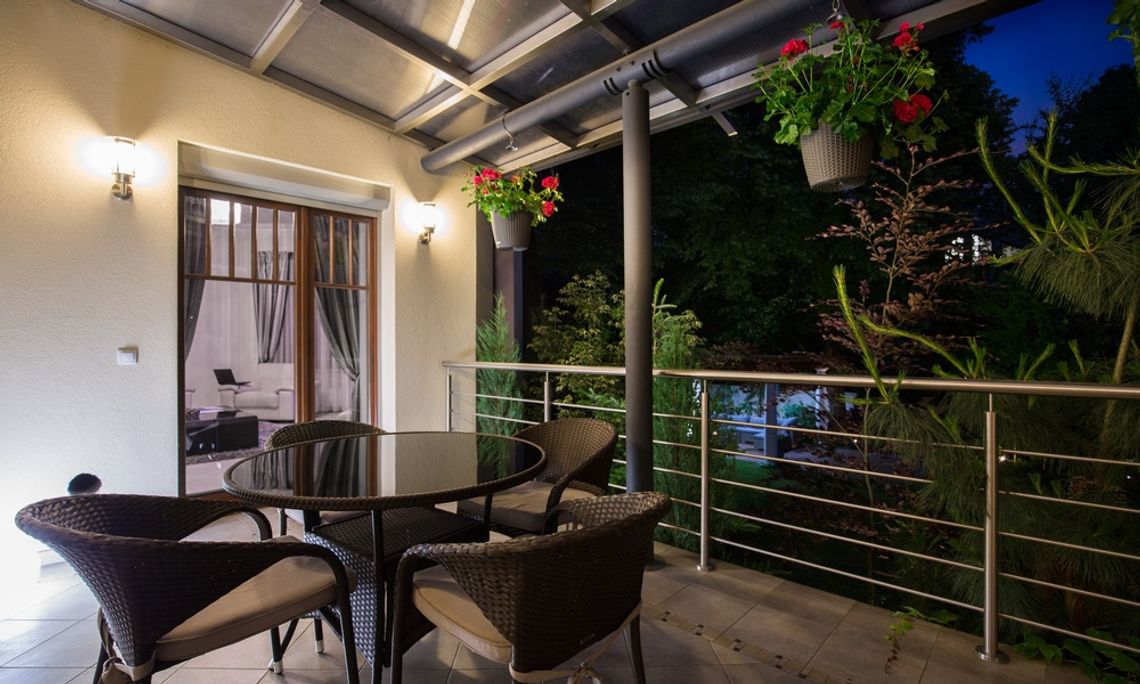 Two sconces illuminate a covered patio at night. A round table with four chairs sits on the tiled patio.