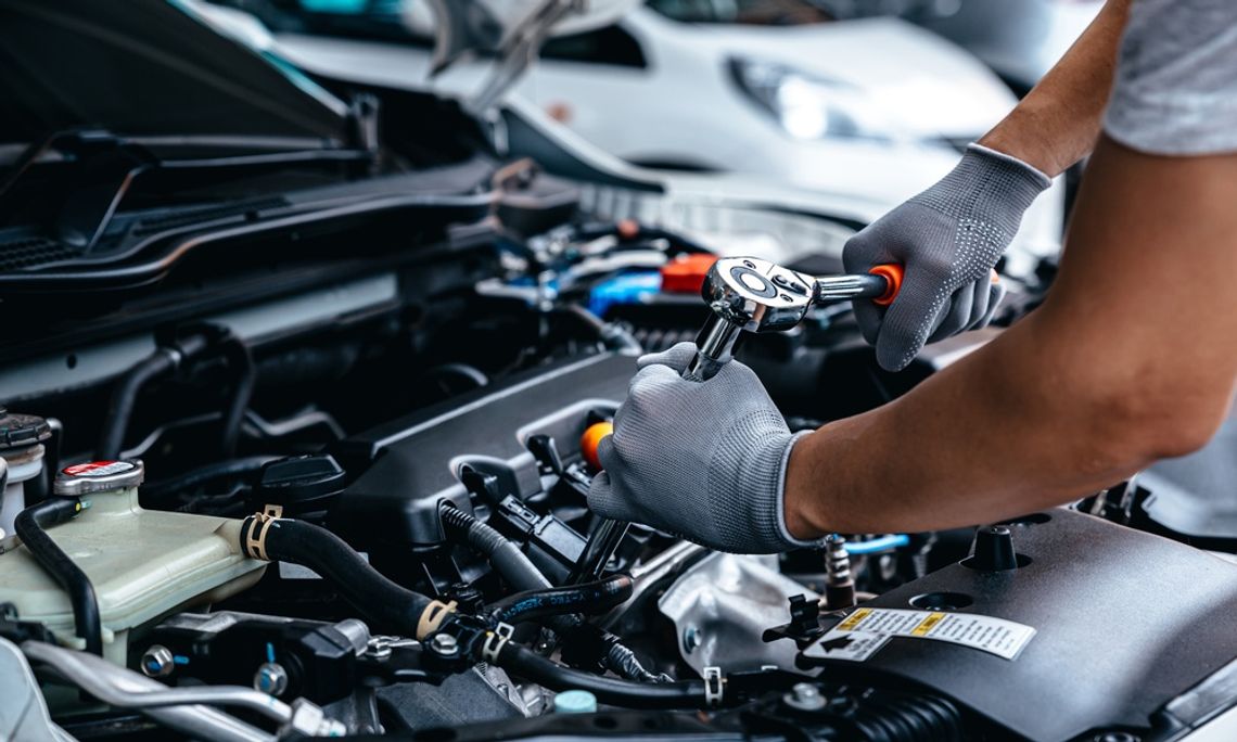 5 Common Car Engine Issues You Shouldn’t Ignore An individual in a gray T-shirt and gray gloves uses a wrench with an orange handle to work on a vehicle engine.