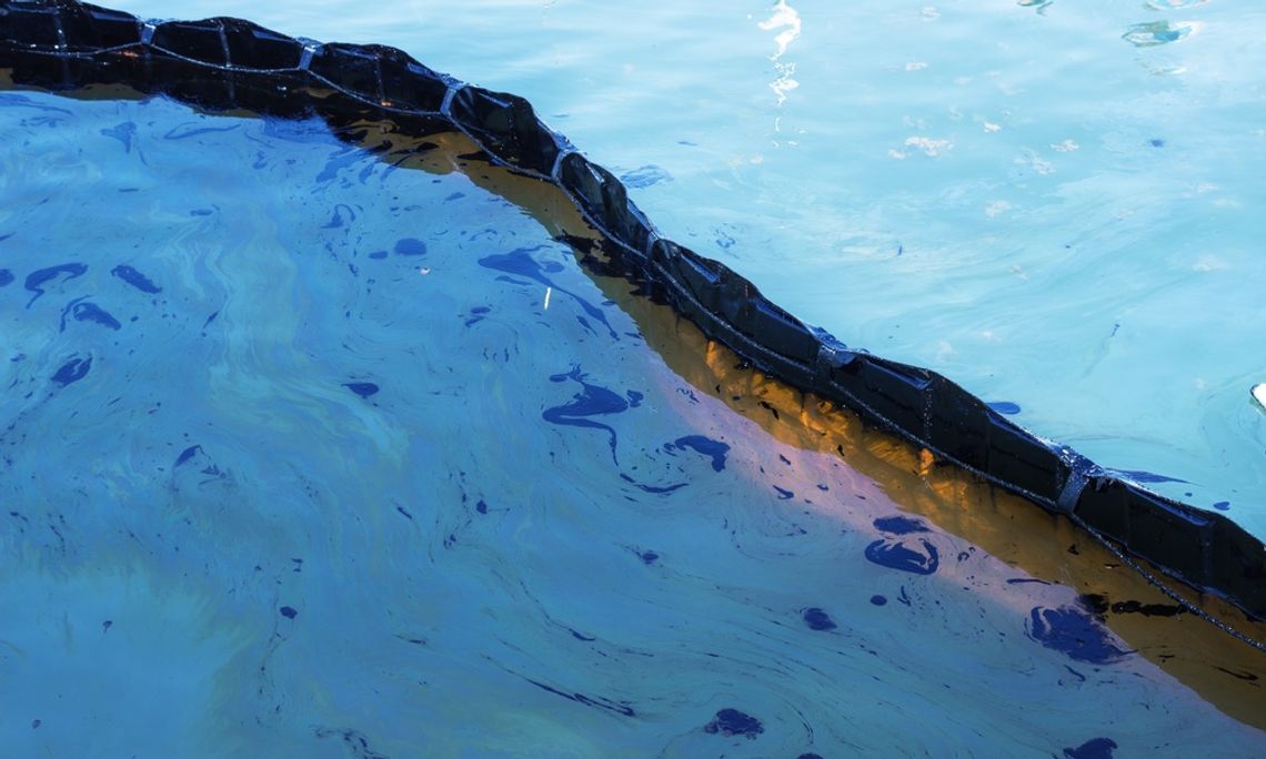 Floating containment boom on water with visible oil sheen, showing pollution control barrier across surface.