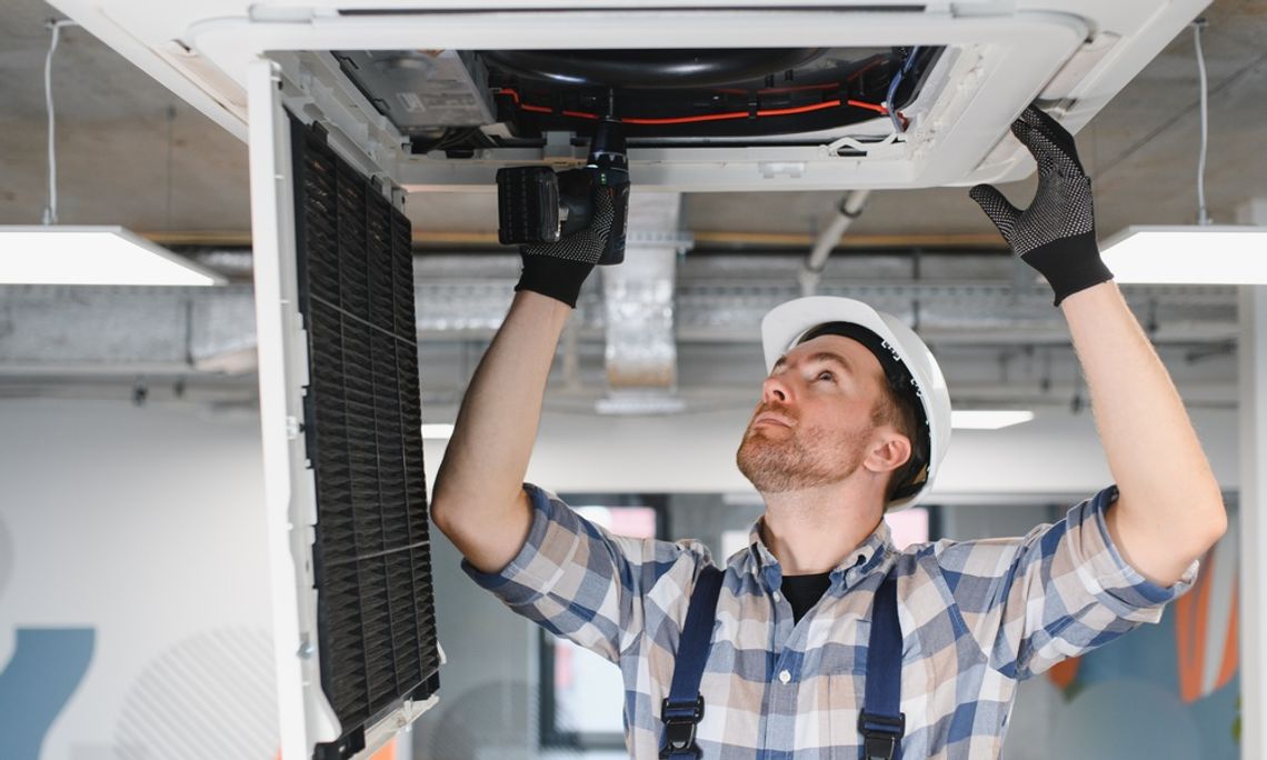 A close-up of an HVAC technician using his tools and repairing an air conditioner unit on the ceiling.