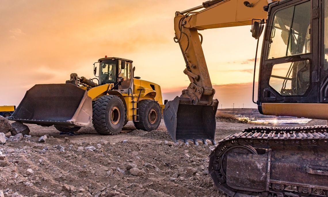 A yellow bulldozer and excavator working on a patch of furrowed, rocky dirt. The sky is orange.