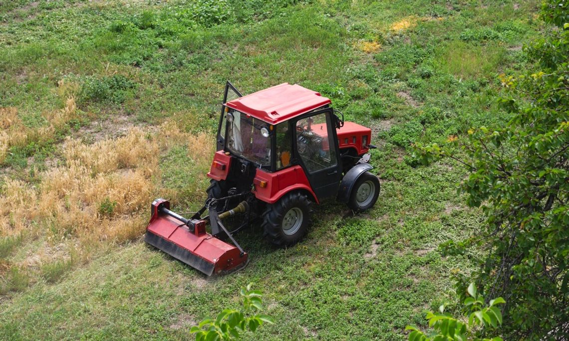 An overhead view of a red tractor with a brush cutter attachment. The tractor is driving through a green field.