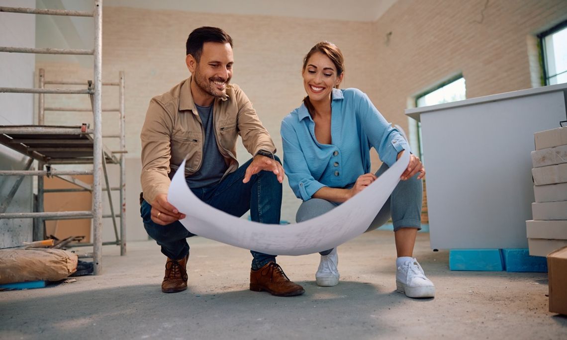 8 Tips for Planning Out Your Home Projects for Next Year Couple reviewing building plans together while renovating a home, surrounded by construction materials and scaffolding.