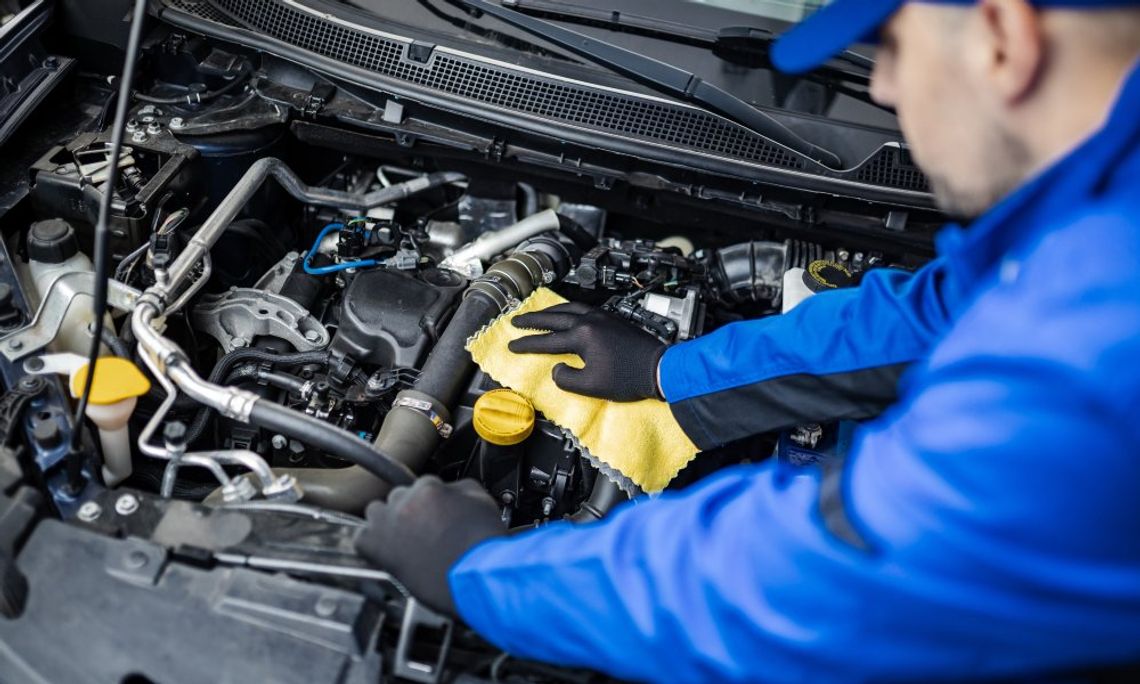 A mechanic in a blue uniform working under the hood of a car to diagnose and correct an issue with the powertrain system.