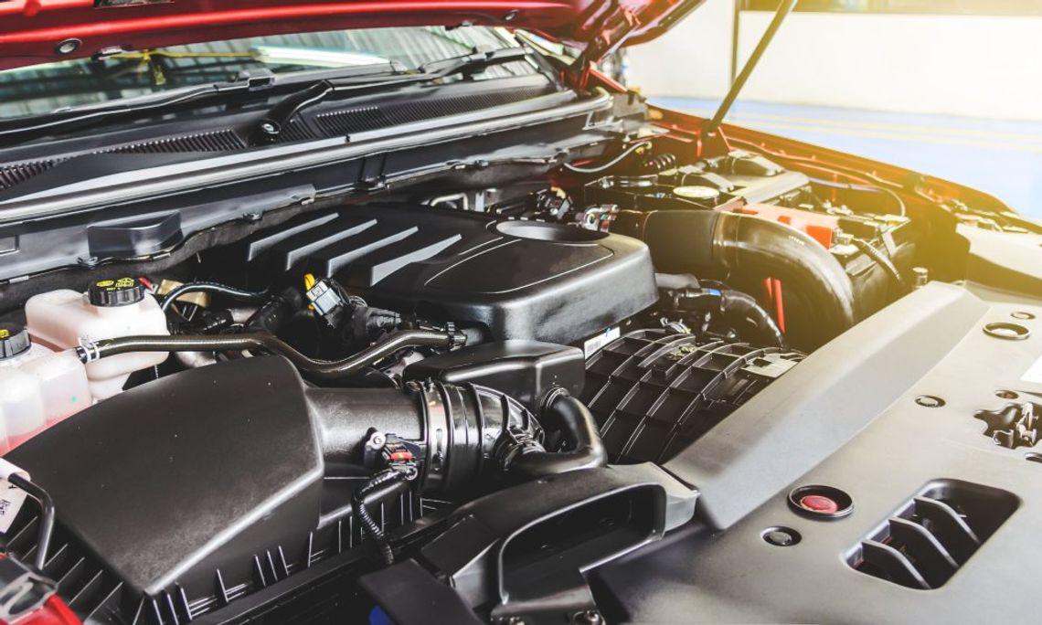 A close-up of the exposed engine bay of a red pickup truck. The displayed components appear clean and new.