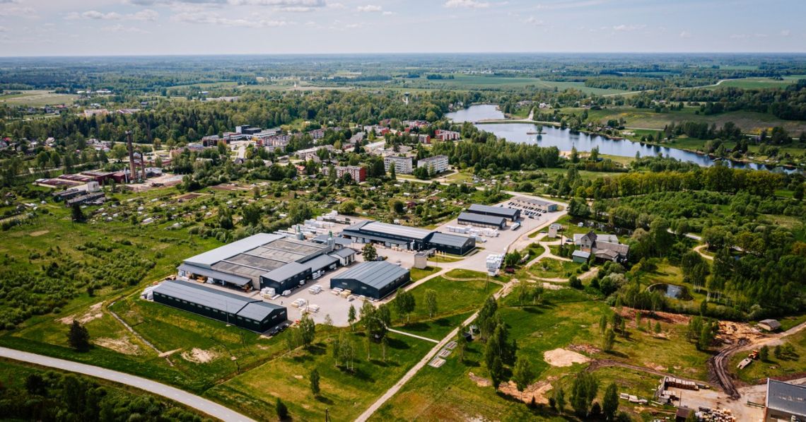Aerial view of a small town surrounded by green fields, with industrial buildings and a lake nearby.