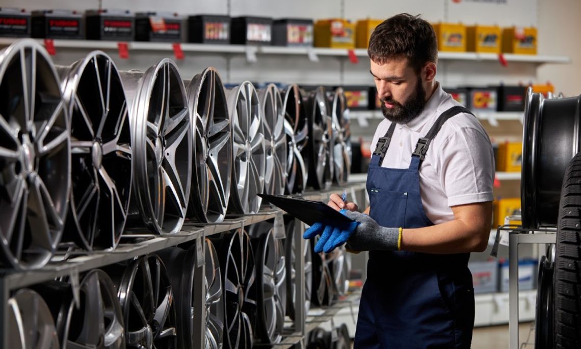 Benefits of Buying Aftermarket Automotive Parts An employee at an auto parts store writing on a clipboard while standing in front of a huge shelf full of car rims.