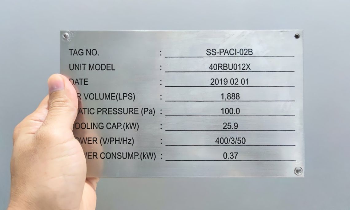 Best Materials for Long-Lasting Equipment Labels A close-up view shows a person holding a stainless steel nameplate that lists items such as tag no., date, and unit model.