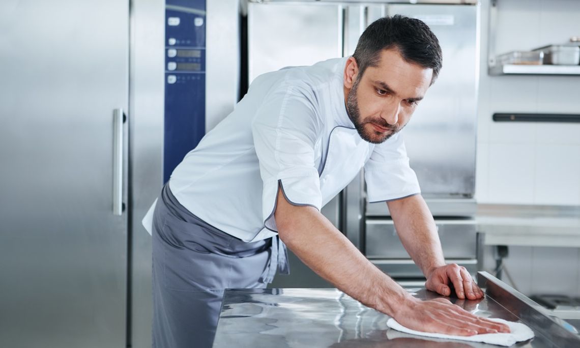 Best Practices for Commercial Kitchen Cleaning Chef wipes down a stainless steel prep table with a cloth inside a clean, professional commercial kitchen.