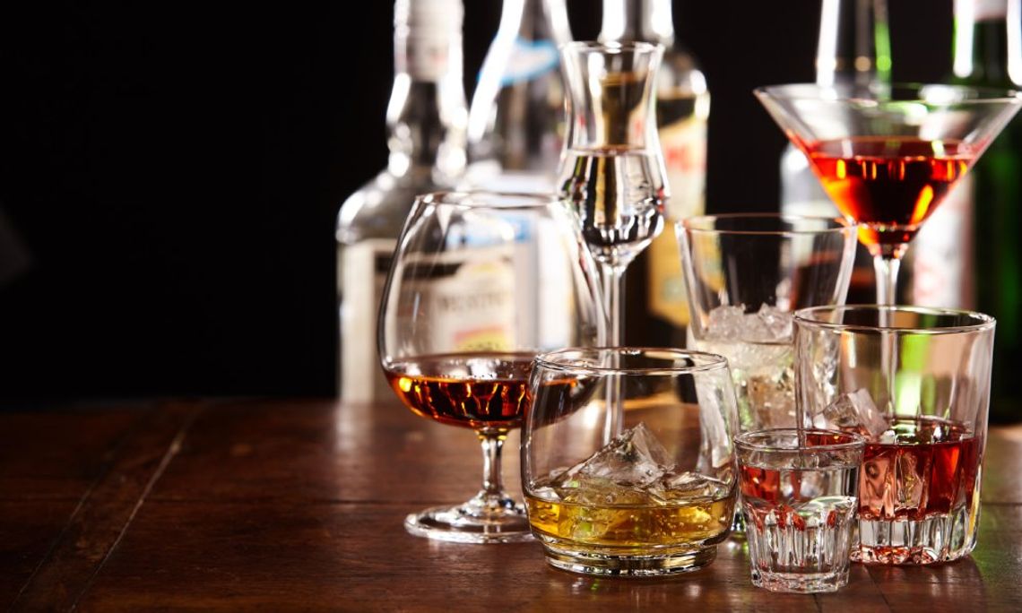 An assortment of cocktails in different glasses, from shot glasses to martini glasses, on a wooden table.