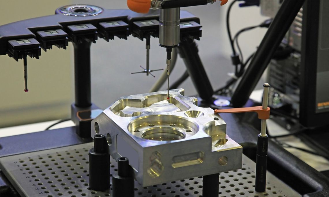 A CMM machine with multiple stylus attachment types measures a machined metal part on a fixture plate.