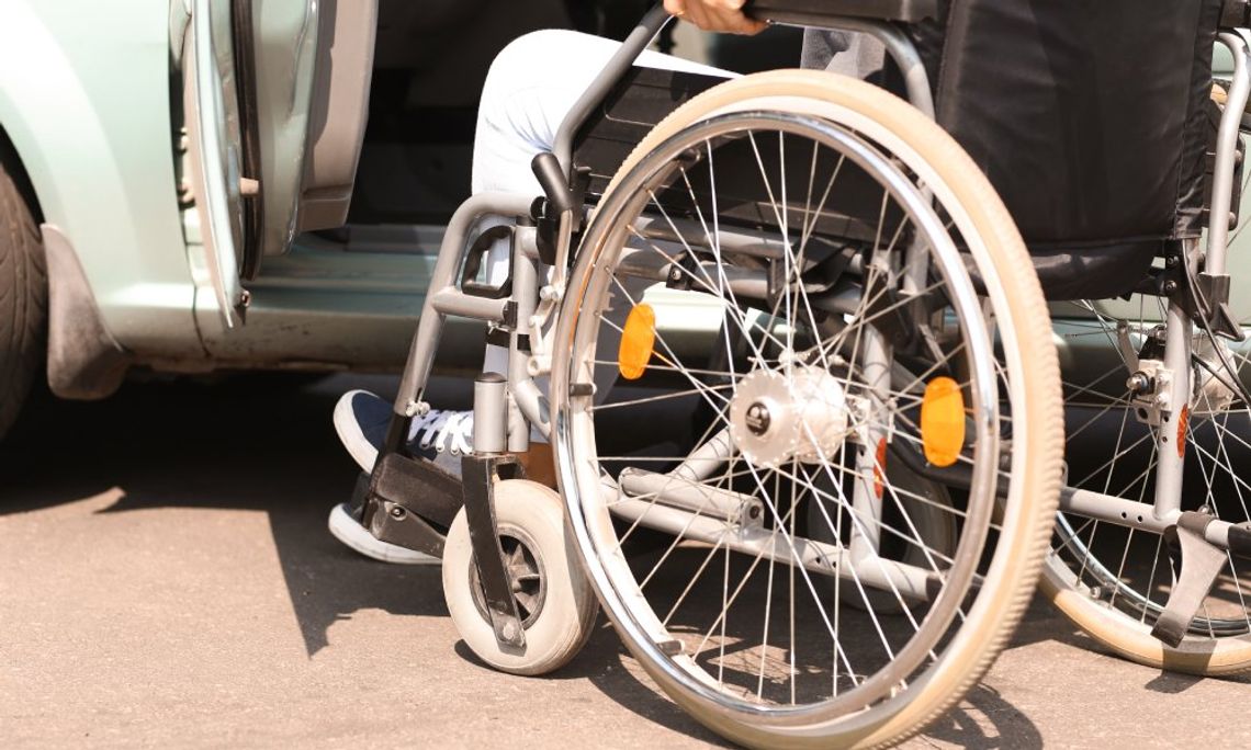 A close-up of the wheels of a wheelchair as the user approaches the open door of a car's driver's side.