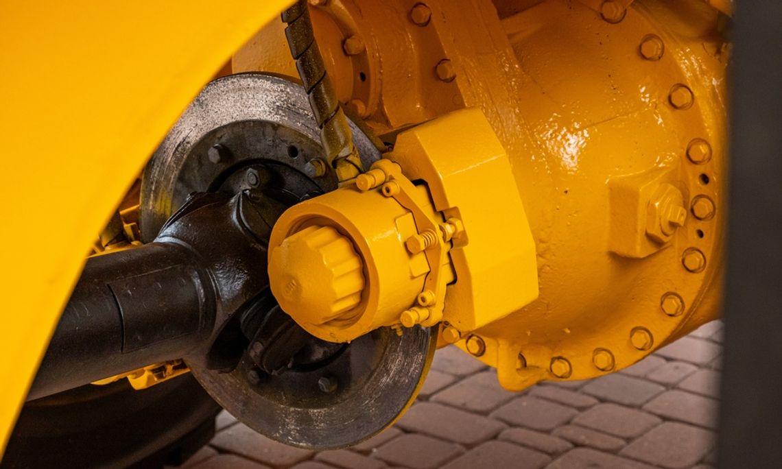 Common Brake Problems in Heavy-Duty Equipment A yellow industrial machinery axle assembly with a metal brake disc, black driveshaft, and large bolted housing.