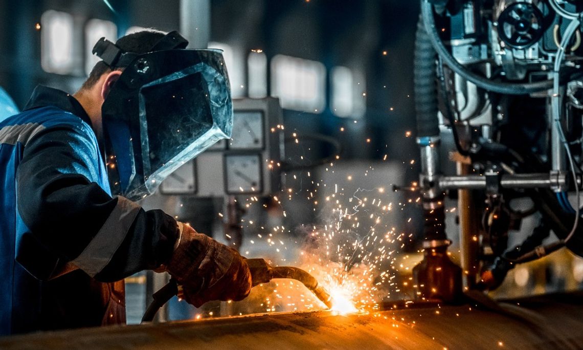 Common Causes of Manufacturing Bottlenecks A man in a welder's mask using a welding torch to connect two different sections of a large pipe together.