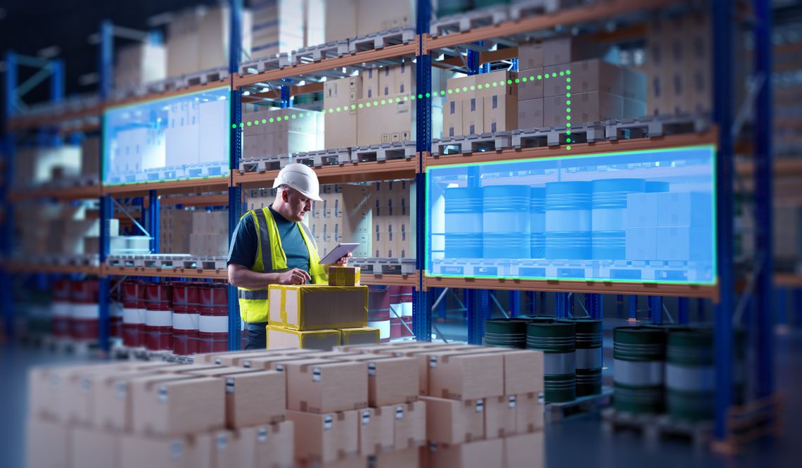 A warehouse worker in a hard hat and yellow vest uses a tablet. Blue graphics cover the shelves of inventory.