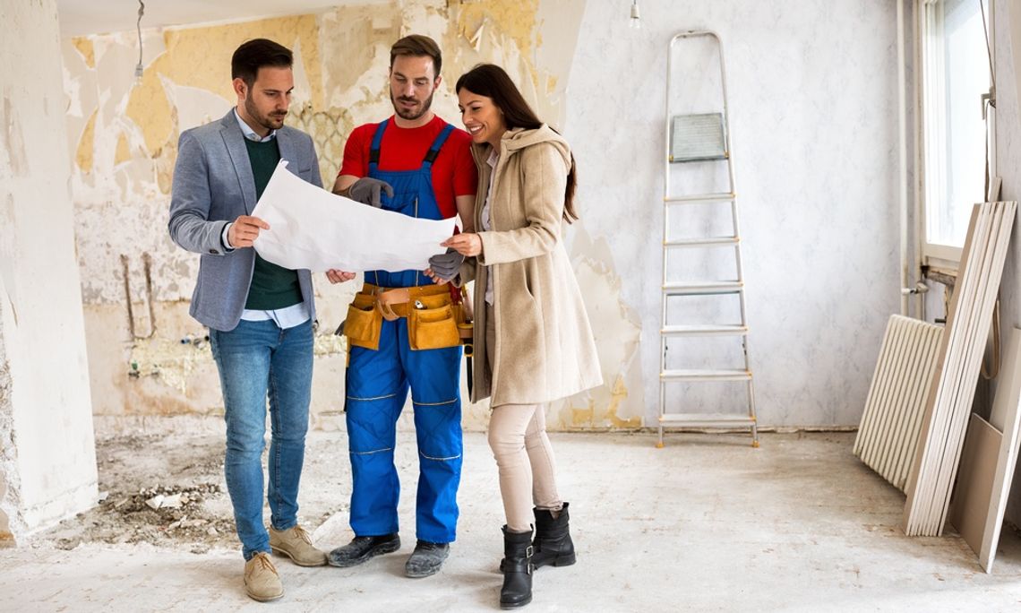 Three people looking at the blueprints for a house. They are standing in a room that is under renovation.