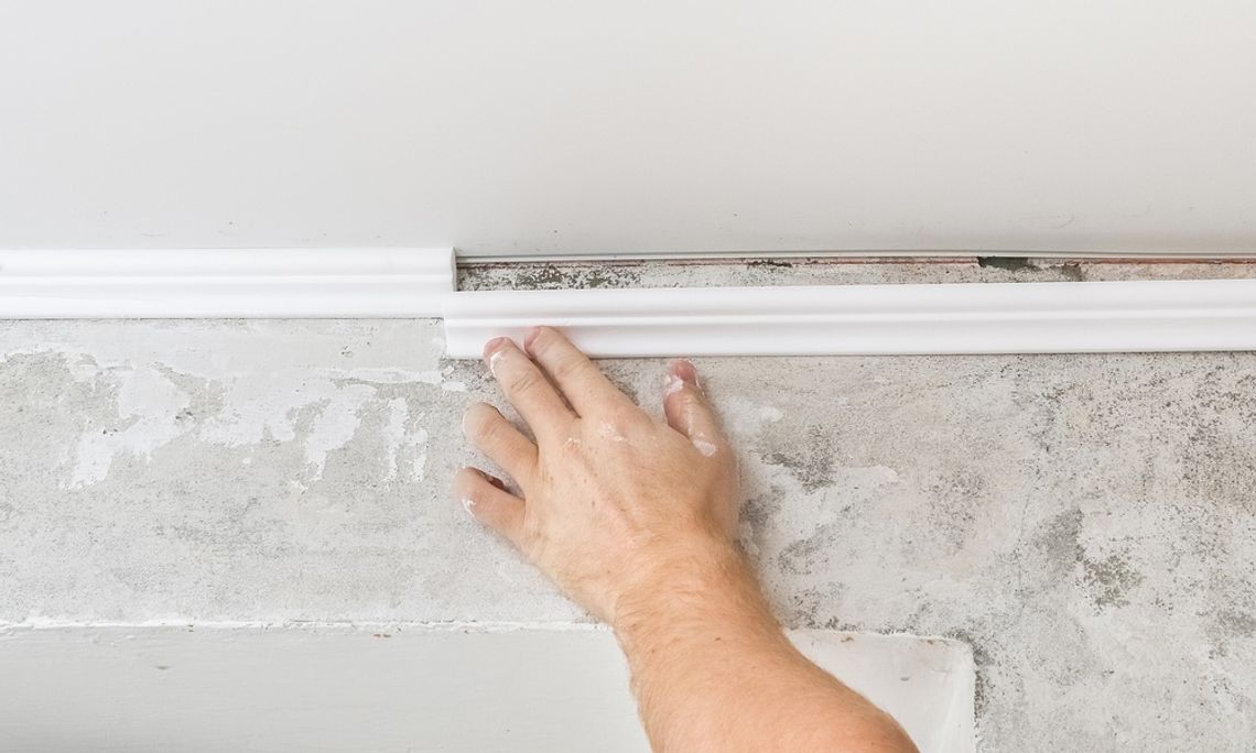 Crown Molding Tips for First-Time Installers A person's hand reaches up to push crown molding into place. The molding is white and matches the ceiling.