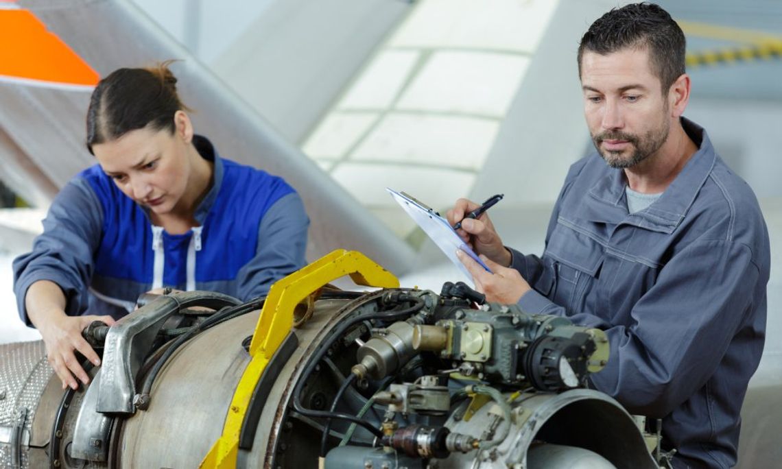 Cutting Tool Innovations for Aerospace Manufacturing A woman grasps the exposed components of a machine while a man inspects them and writes notes on a clipboard.