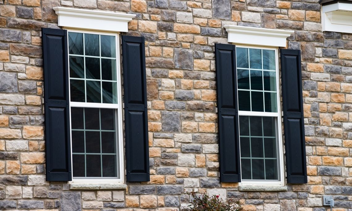 The exterior of a home with full brick siding and two rectangle single pane windows that have black shutters on each side.