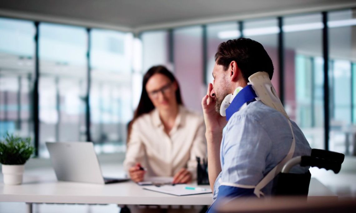A personal injury lawyer at the back of the table with a laptop, sitting with a client who is wearing a neck brace.