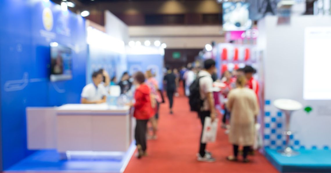 Essential Equipment You Need for Your Exhibition Booth A large crowd of visitors at a trade show gather in a hallway lined with brightly lit exhibition booths.