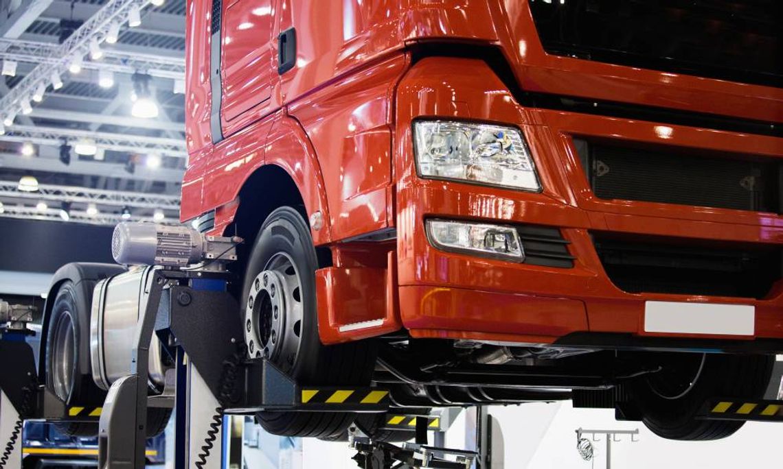 A close-up of a red truck cab resting on a car lift in a large garage, awaiting parts replacements and servicing.