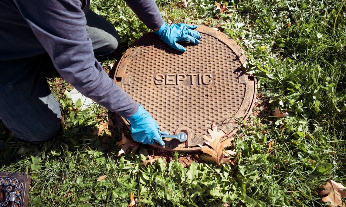A plumber working with gloves on his hands uses a socket wrench to open a manhole cover with the word "Septic" on it.