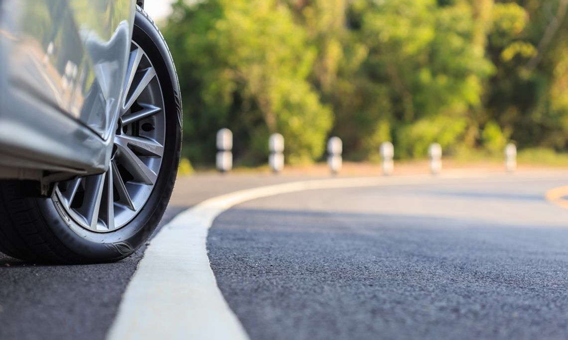 Exploring the Impact of Tires on Road Safety On the side of the road, a car has the front wheel turned out towards the white line. There are trees down the road.