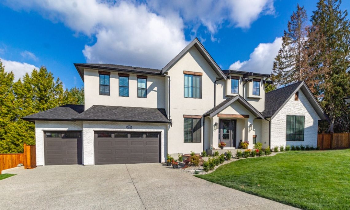 Garage Door Features That Increase Home Value The exterior of a home with a beige facade. The two-door and single-door garage are dark brown with one row of windows.