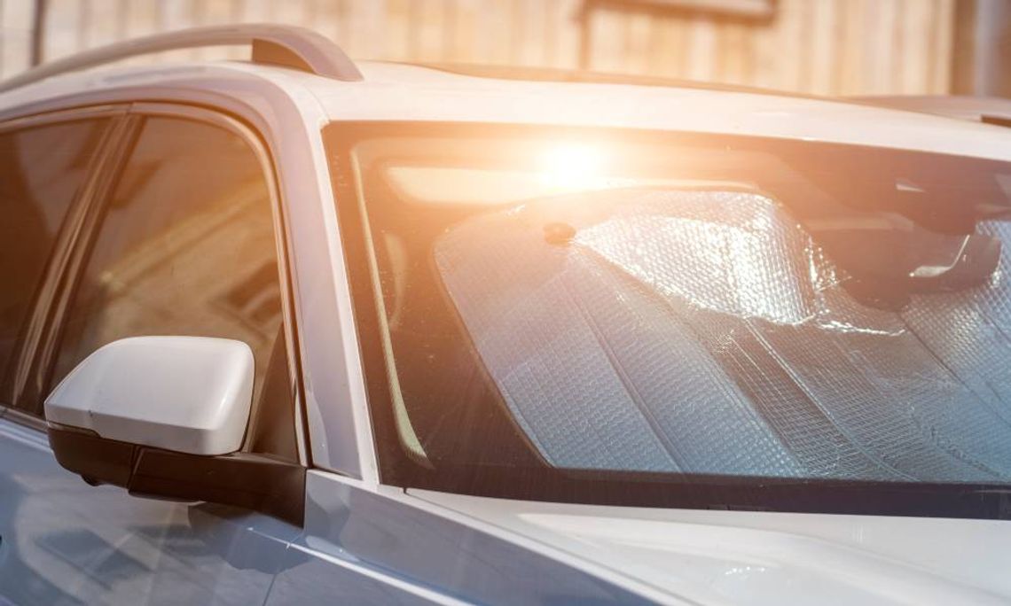 A silver car sits in a parking lot. The sun creates a warm glow and reflects off of the vehicle's sun visor on the windshield.