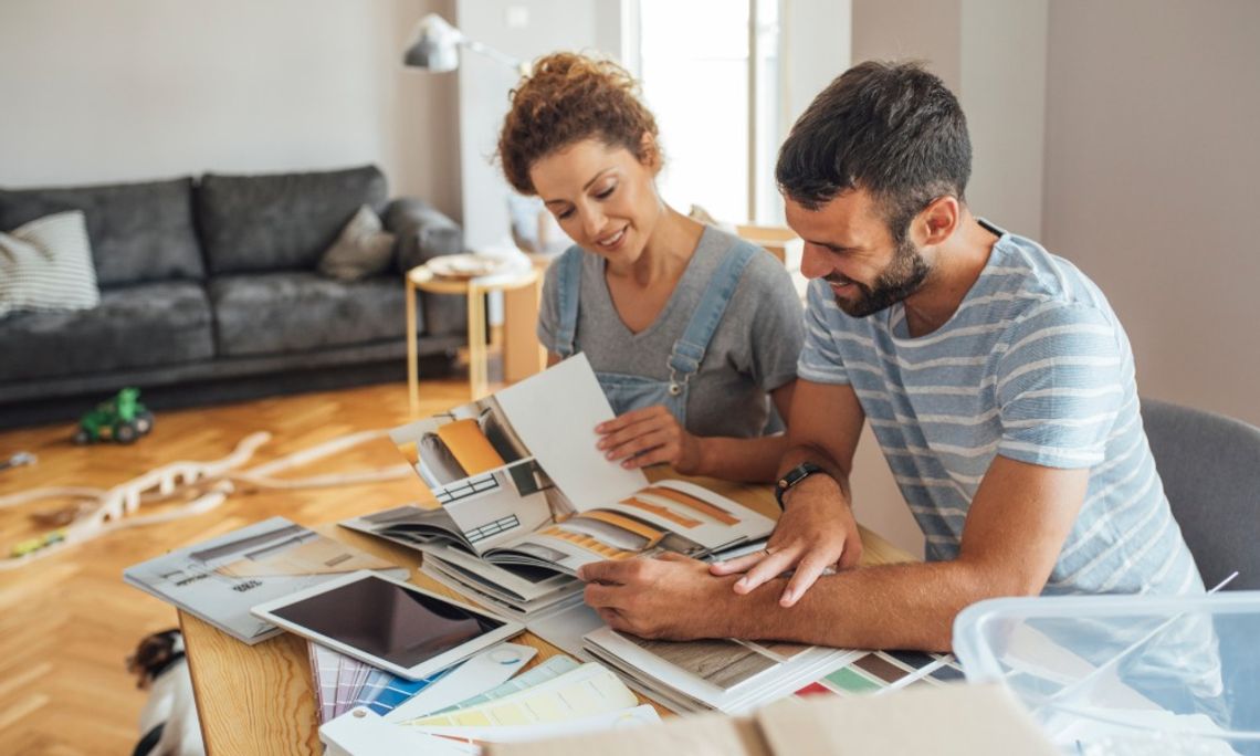 Home Renovation Details That Deserve More Attention A couple sits together at a dining room table to discuss renovation details. The table contains books, plans, and swatches.