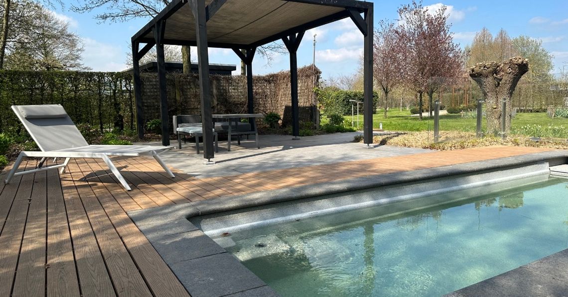 An outdoor living space with a rectangular pool next to an aluminum pergola over a sectional couch and a table.