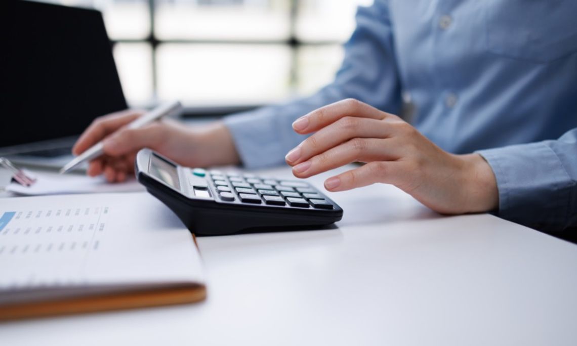How Contractors Can Stay Tax Ready Year-Round Person uses a calculator while reviewing paperwork at a desk, with a pen and laptop nearby in soft focus.