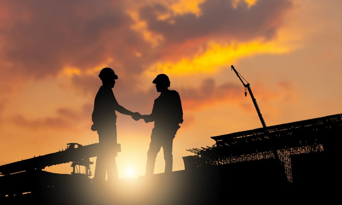 How Engineering Standards Shape Safer Communities Two construction workers standing on a construction site, shaking hands with the sunlight casting a shadow over them.