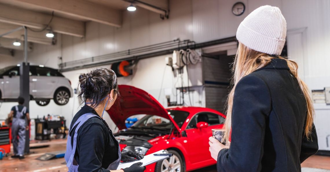 How Local Auto Repair Shops Can Make Better Use of Space A woman in work clothes writing on a clipboard beside another woman near a red car in an auto repair shop.